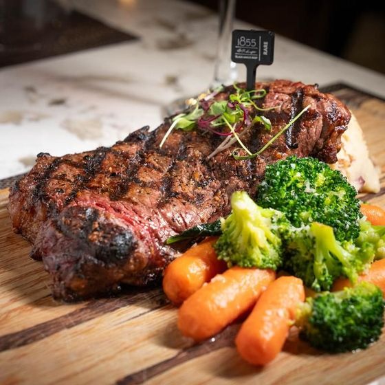 A steak with broccoli and carrots on a wooden cutting board