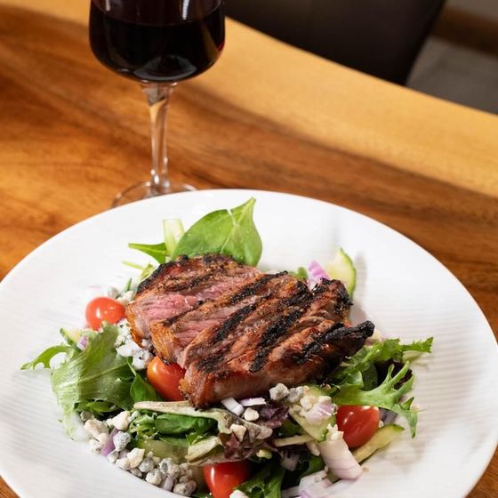 A plate of food with a steak and vegetables next to a glass of wine
