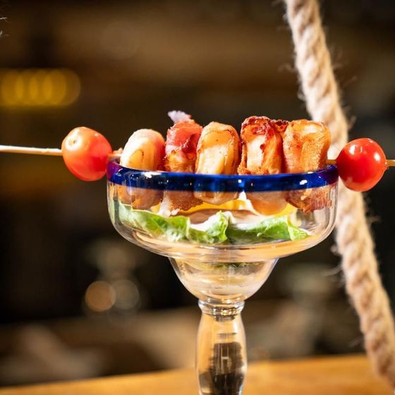 A martini glass filled with shrimp and tomatoes on a rope.