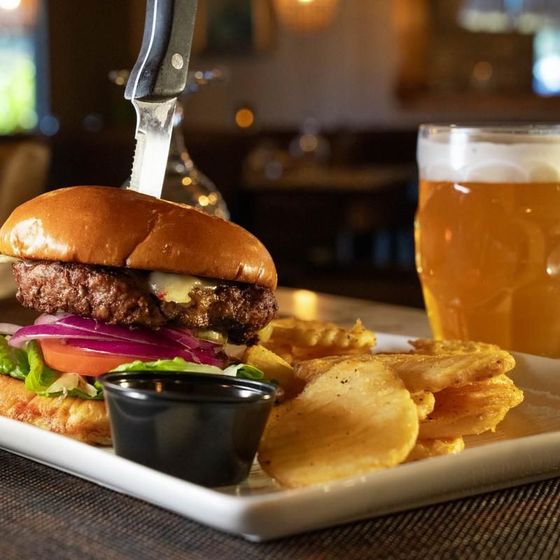 A hamburger and chips on a plate with a glass of beer in the background