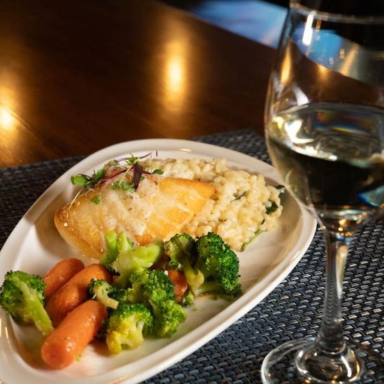 A plate of food with broccoli and carrots next to a glass of wine