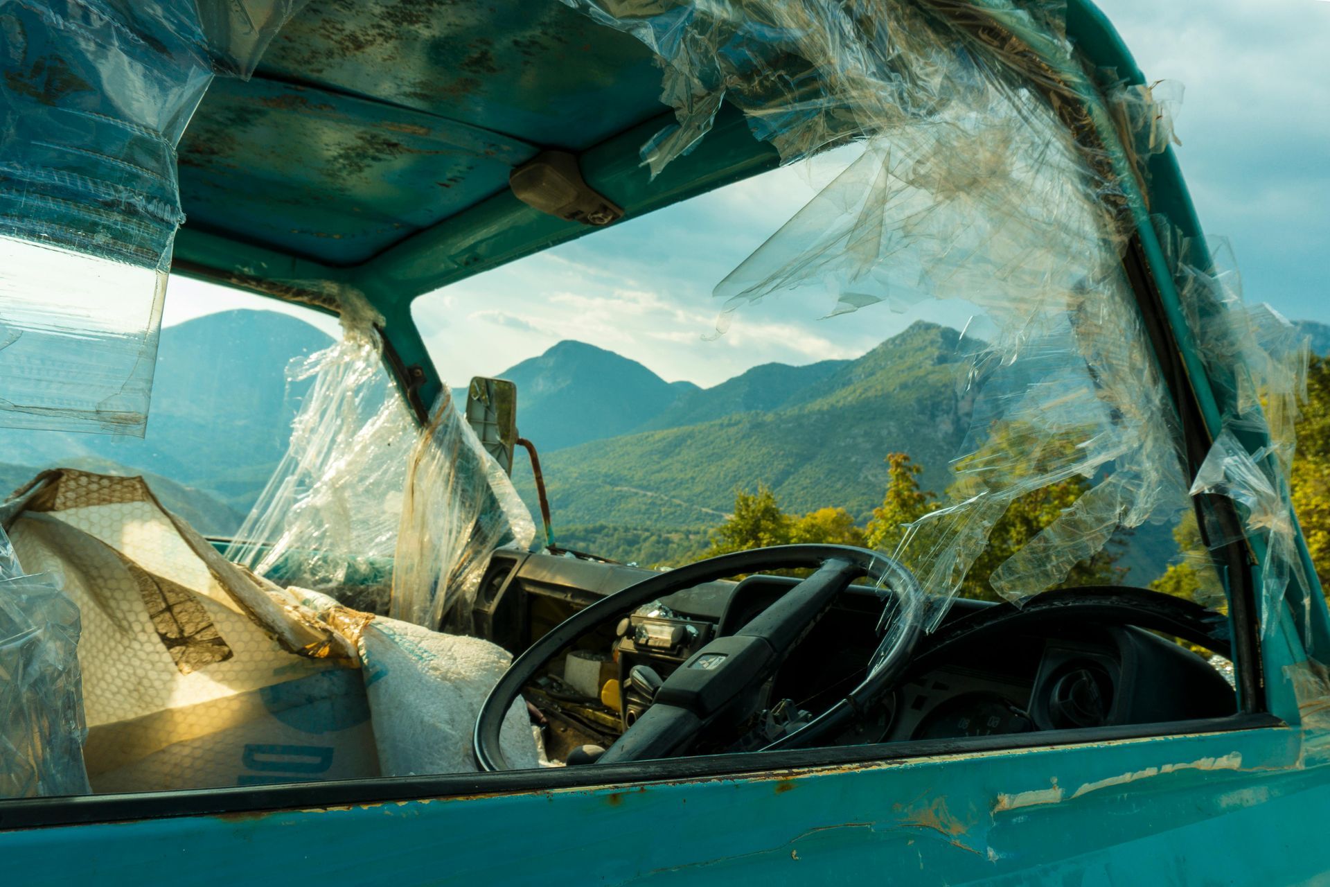 Broken windshield of a turquoise truck with mountain view in background.