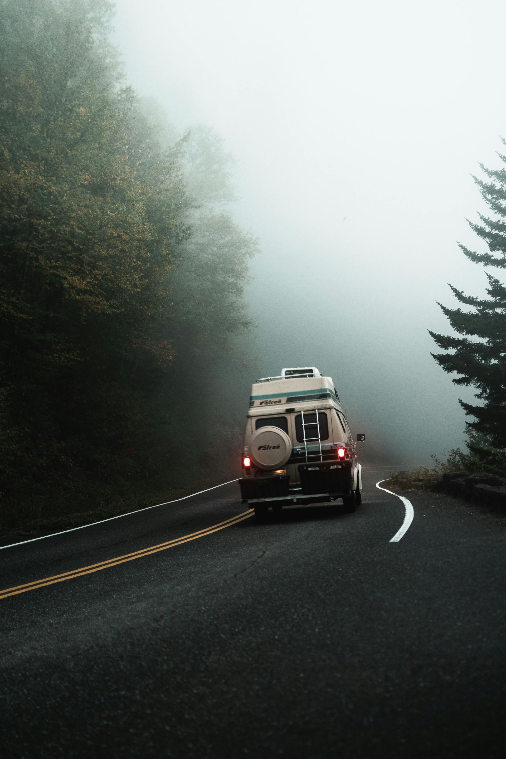 A scenic road with trucks and cars travelling through a mountainous landscape, lined with tall trees