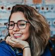 A woman wearing glasses is smiling with her hand on her chin.