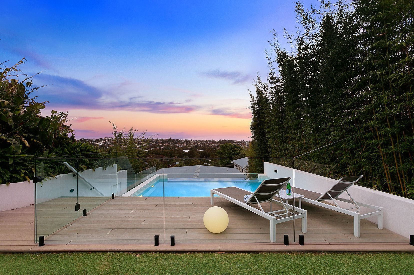 Swimming pool with deck and lounge chairs overlooking a city skyline at dusk.