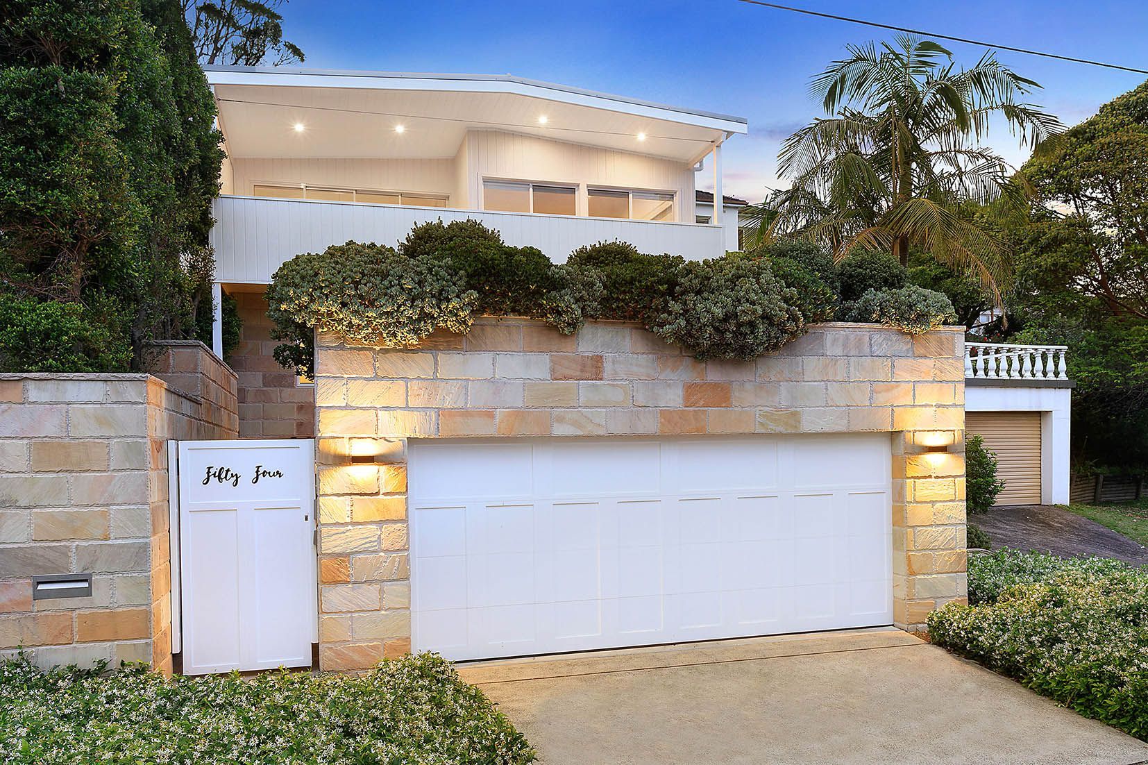 White house with garage door and stone wall. Landscaping and greenery.