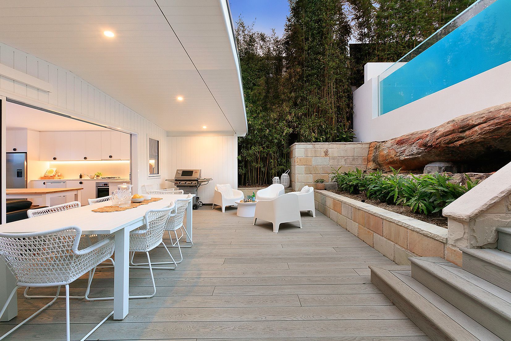 Patio with a long white table and chairs, a grill, and a pool with blue water.