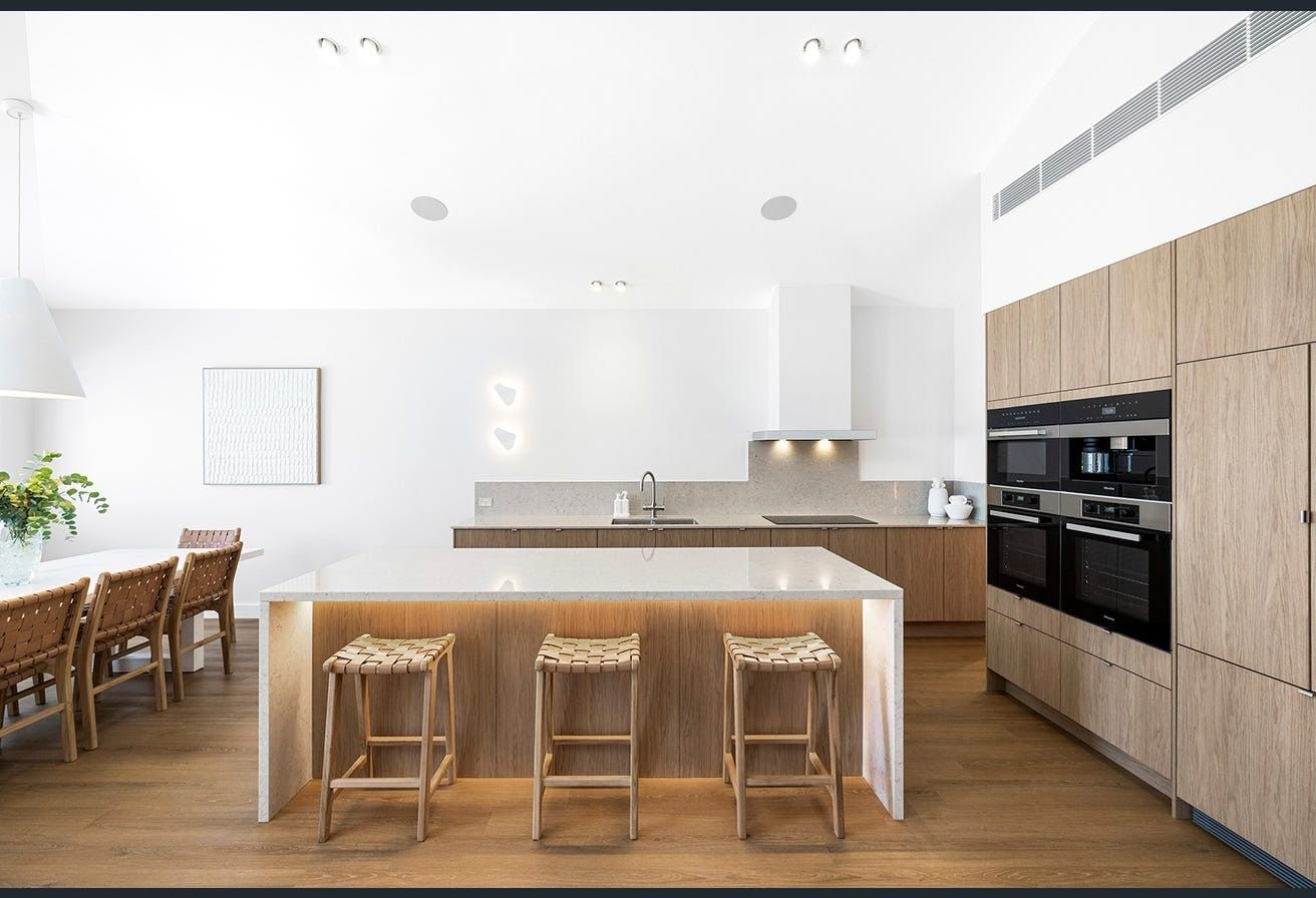 Modern kitchen with light wood cabinets, white island with stools, and dining table.
