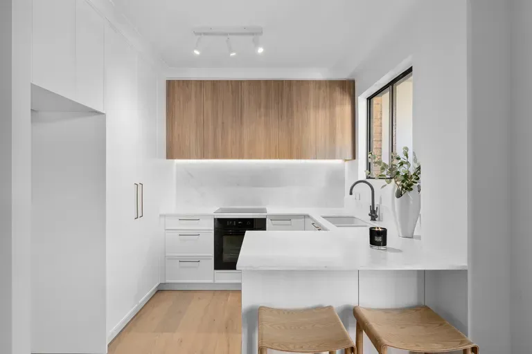 Modern, minimalist kitchen with white cabinets, wood paneling, and a small breakfast bar.