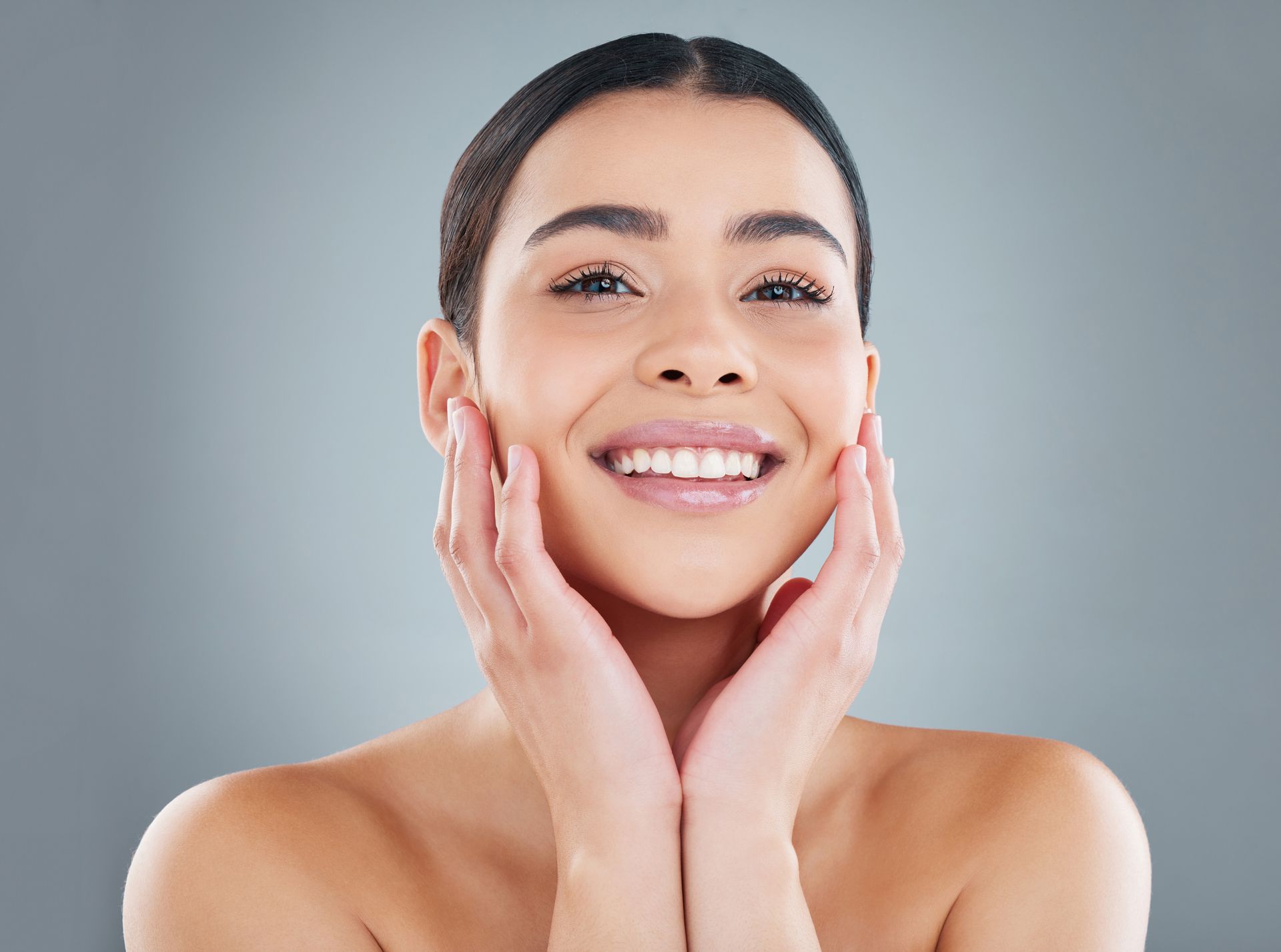 A woman is smiling and touching her face with her hands.