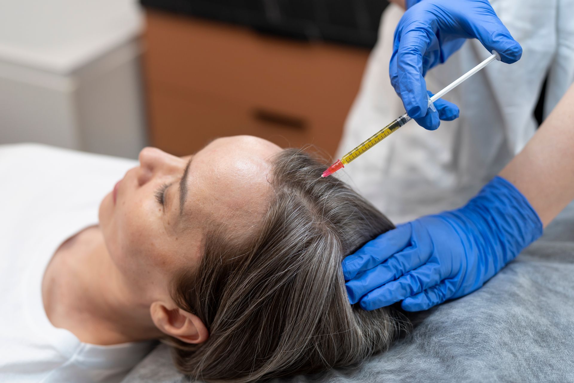 Woman lying down while a medical professional injects a substance into her scalp, likely for hair re
