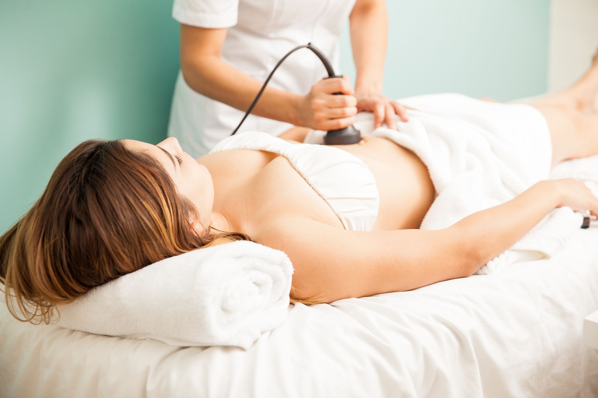 Woman in a towel or robe receiving a cosmetic ultrasound or body contouring treatment on her abdomen