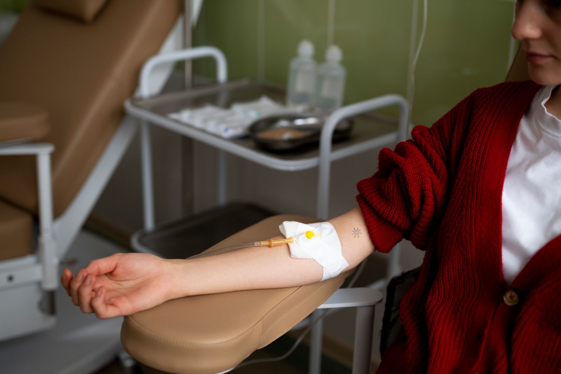 Person sitting in a clinic chair receiving an IV drip in their arm, with medical supplies in the bac