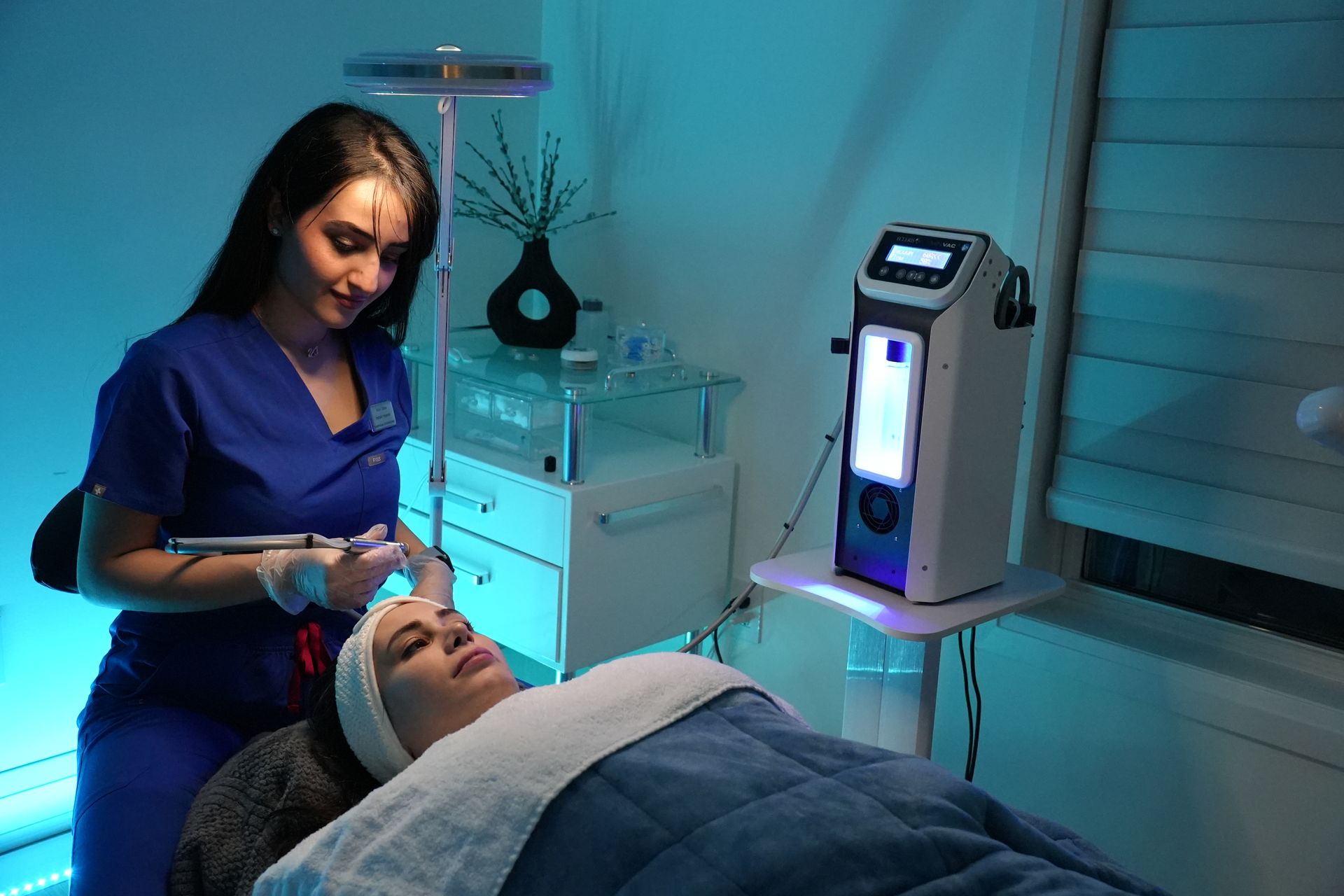 Woman giving a facial treatment to a client in a spa, under blue lights.