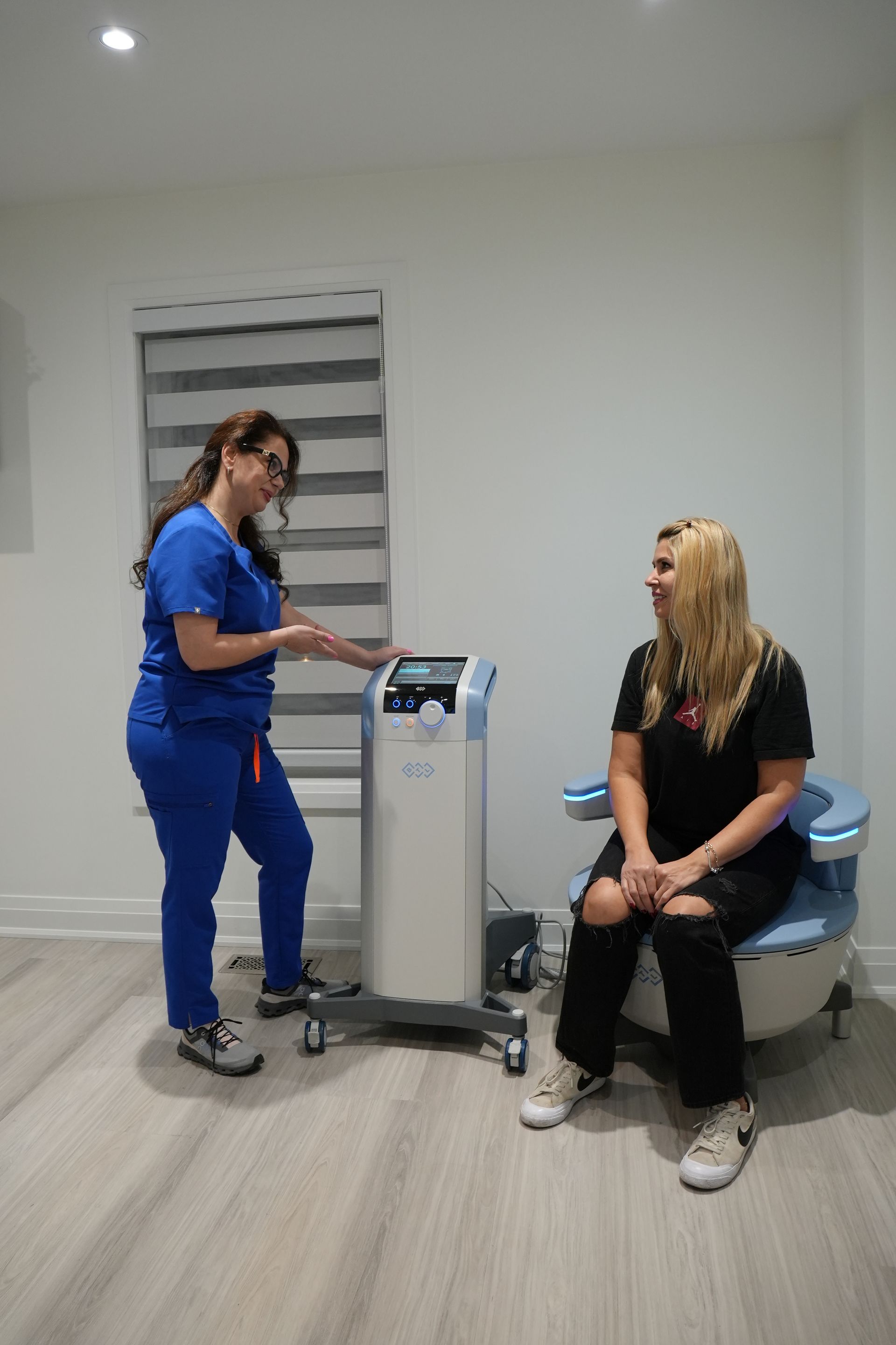 A nurse is standing next to a woman sitting on a chair in a room.