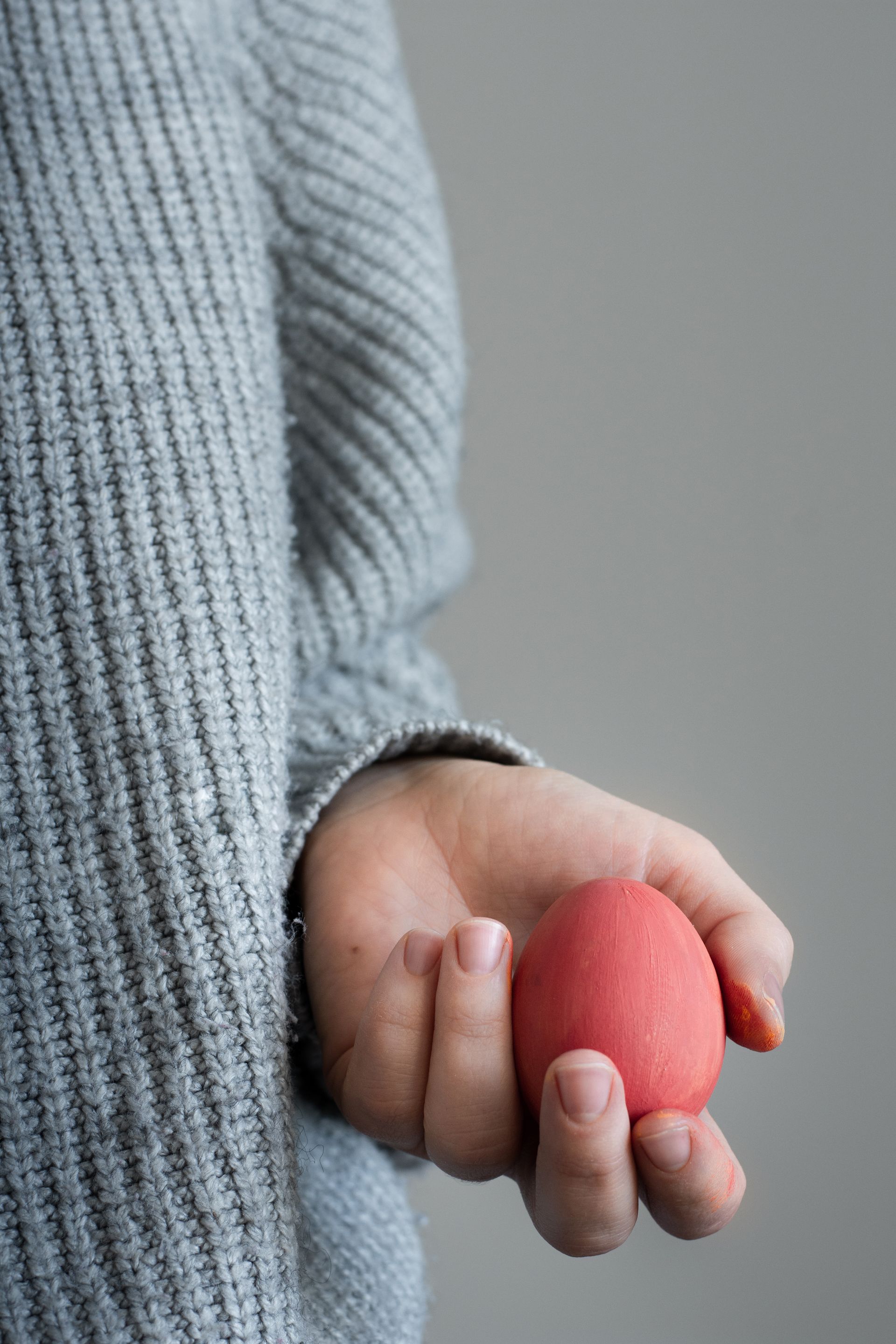 A person is holding a red egg in their hand.