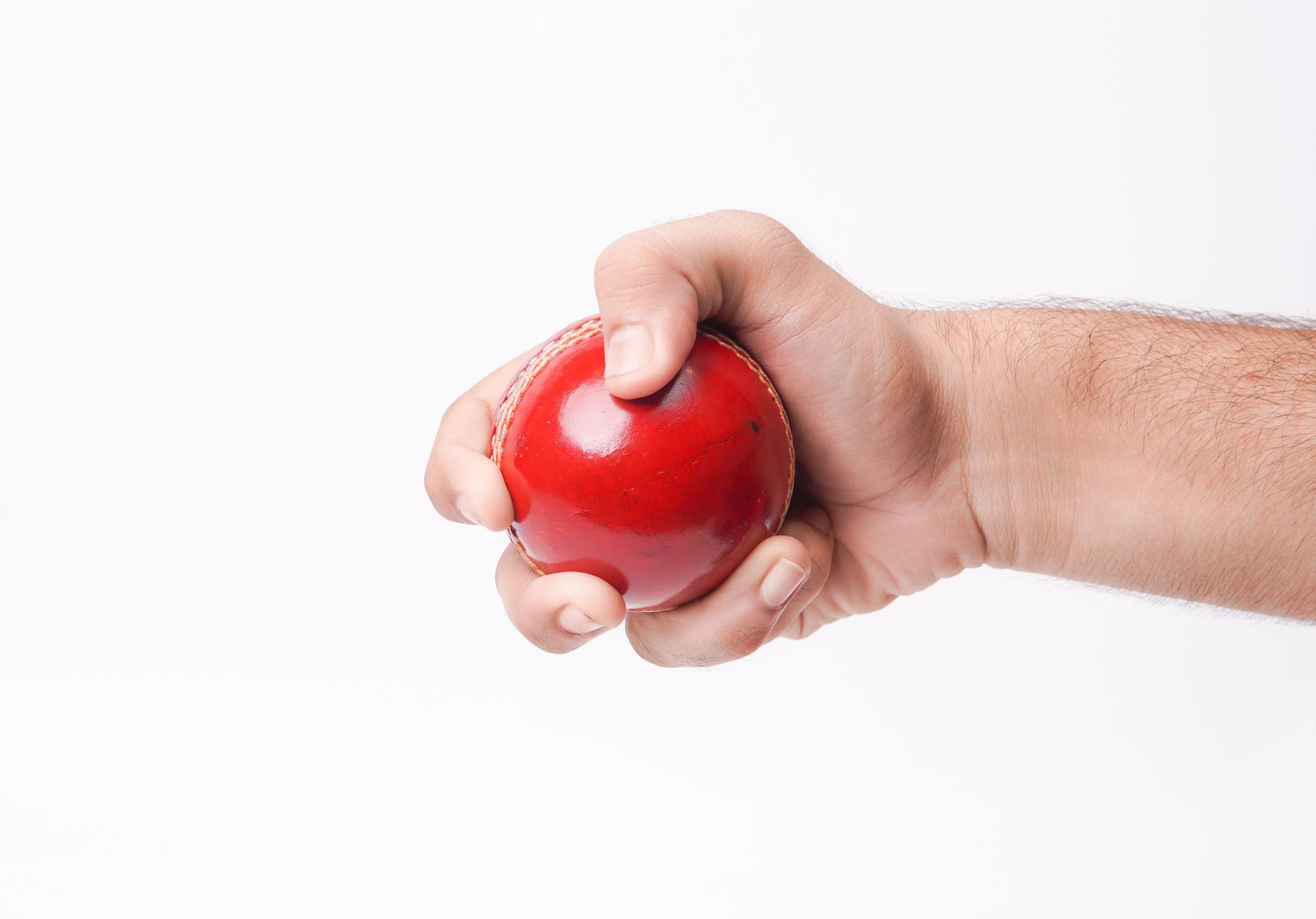 A man is holding a red cricket ball in his hand.