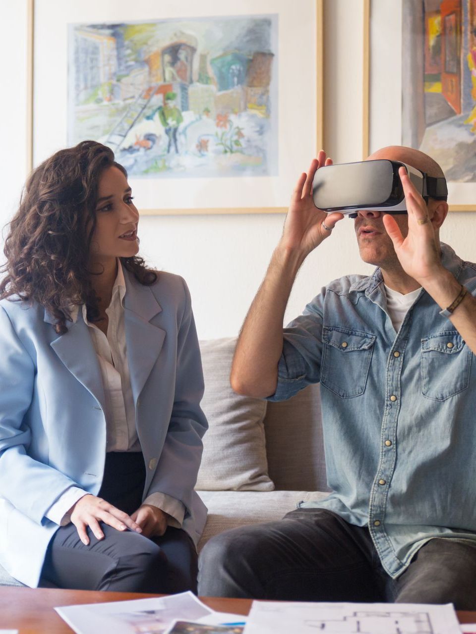 A man and a woman are sitting on a couch and the man is wearing a virtual reality headset.