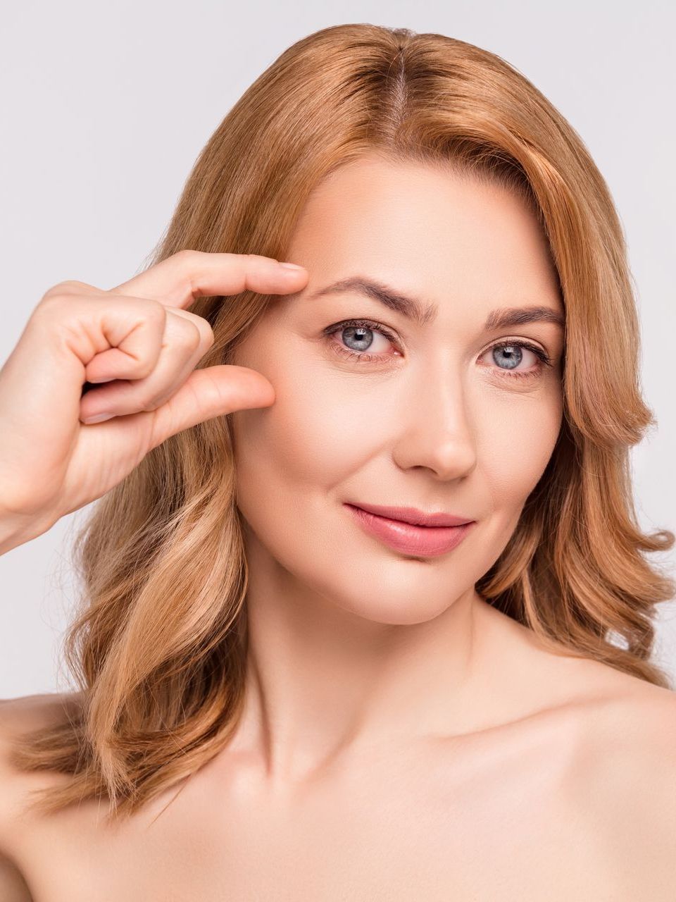 A woman is pointing at her eyebrow with her finger.