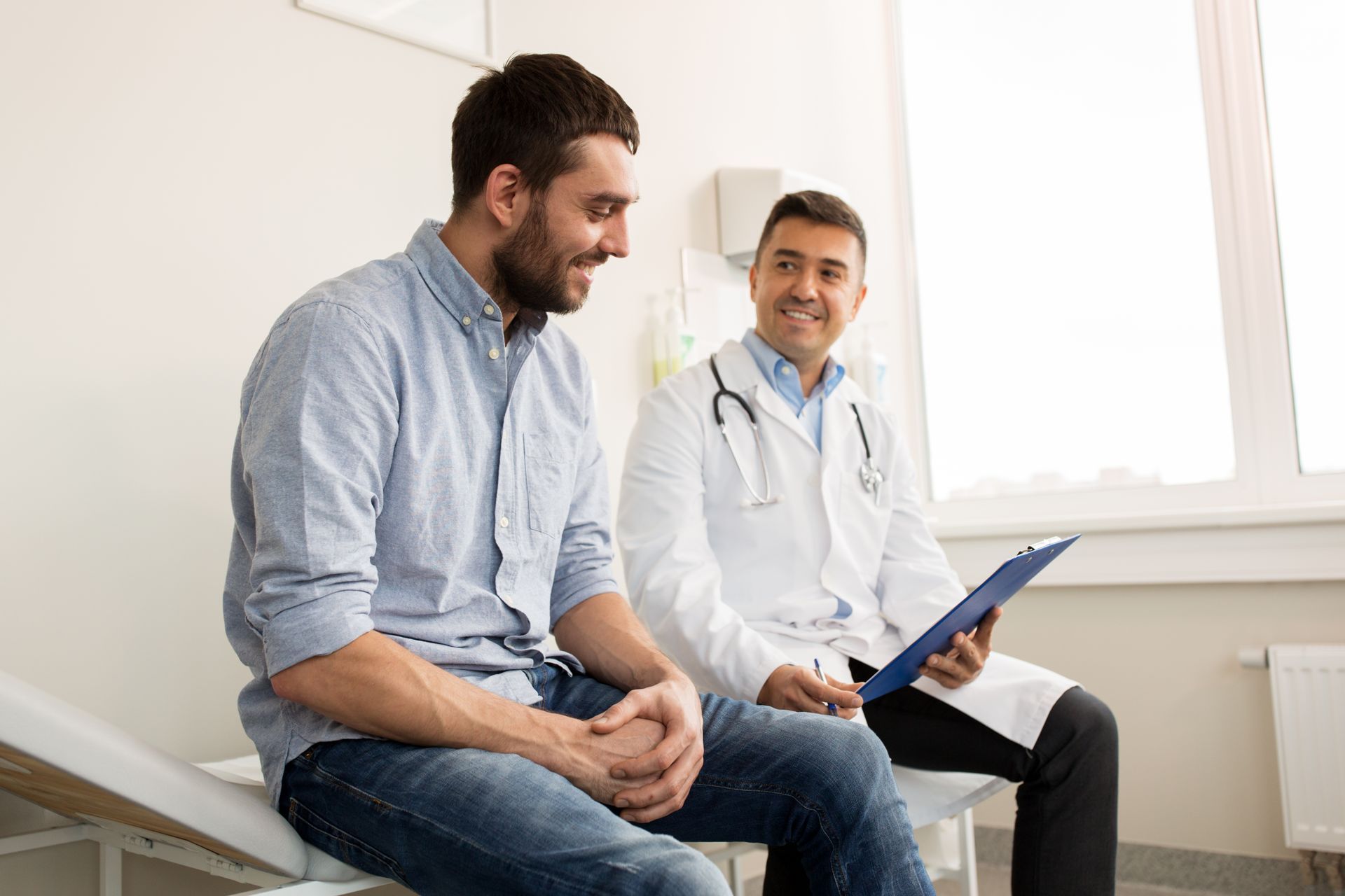 A man is sitting on a bed talking to a doctor.