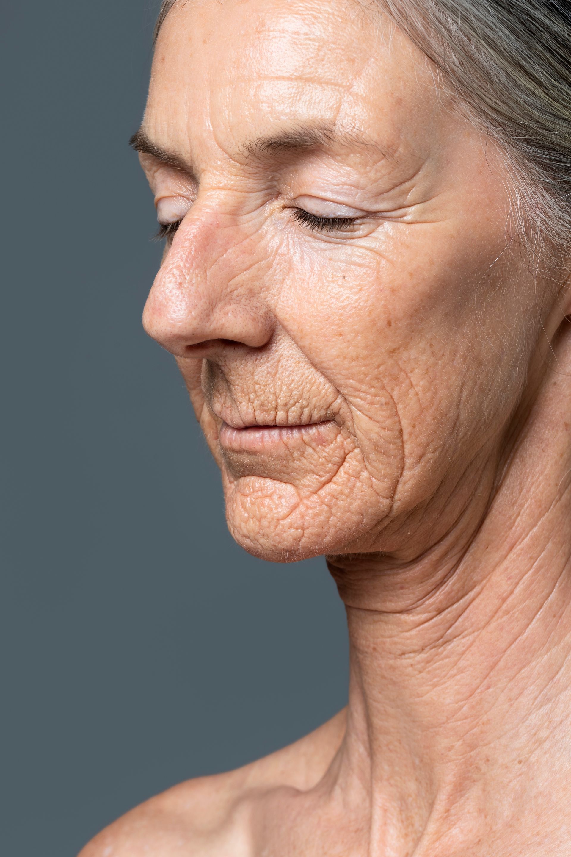 A close up of an older woman 's face with wrinkles on a gray background.