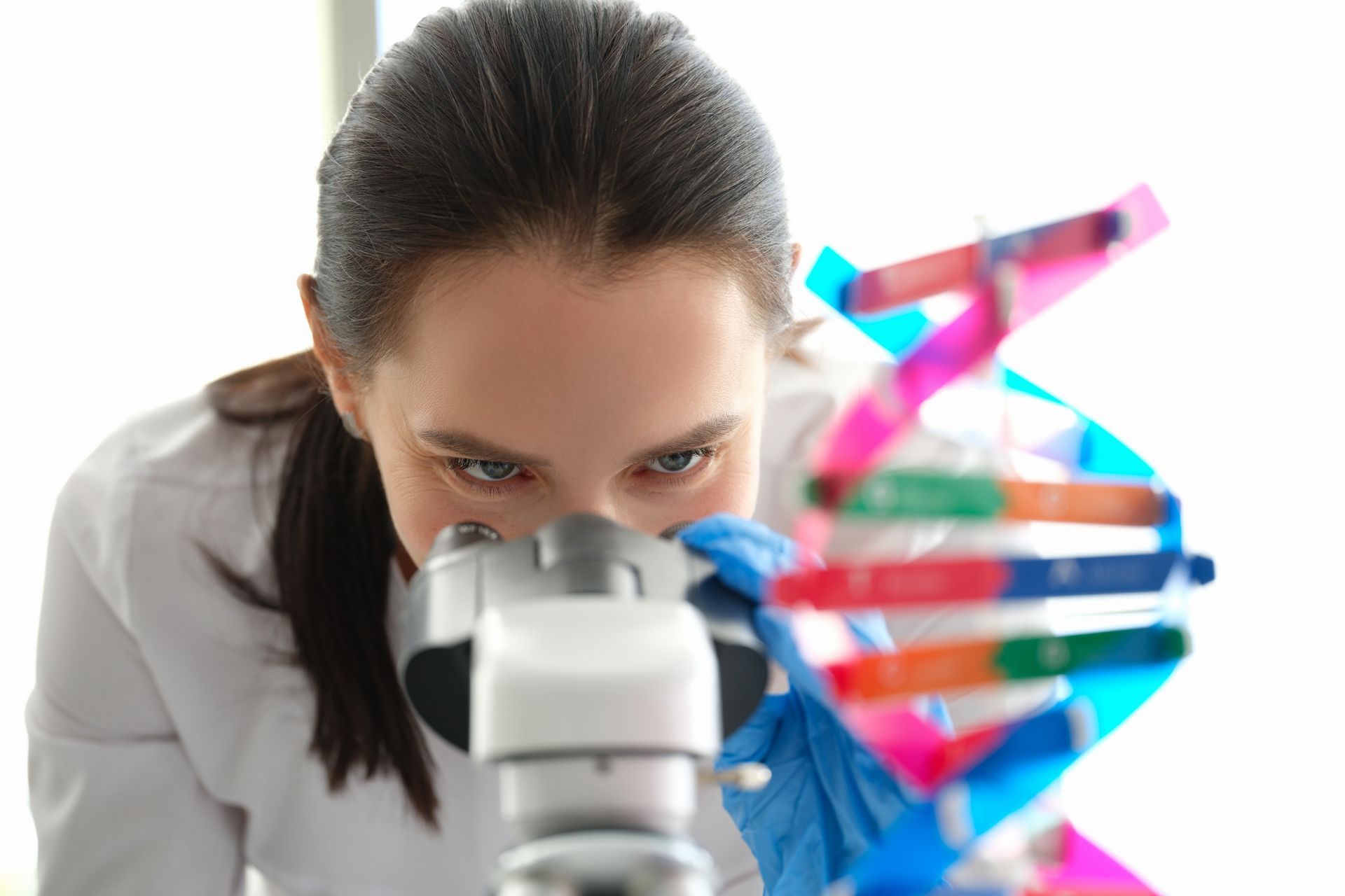 A woman is looking through a microscope at a model of a dna structure.