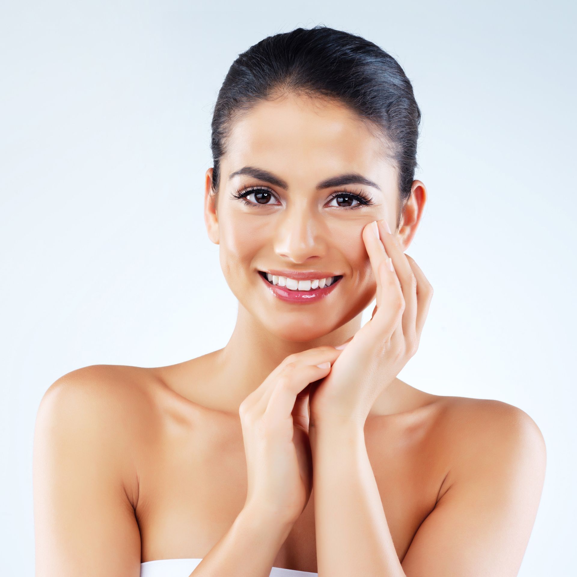 A woman is smiling and touching her face with her hands.