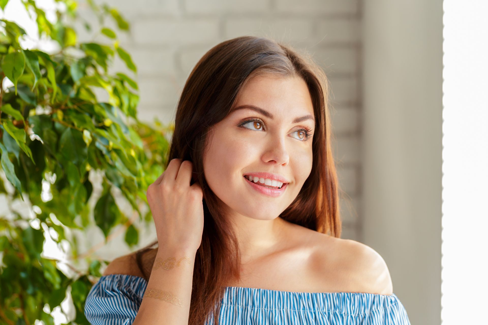 A woman in a blue off the shoulder top is smiling and touching her hair.