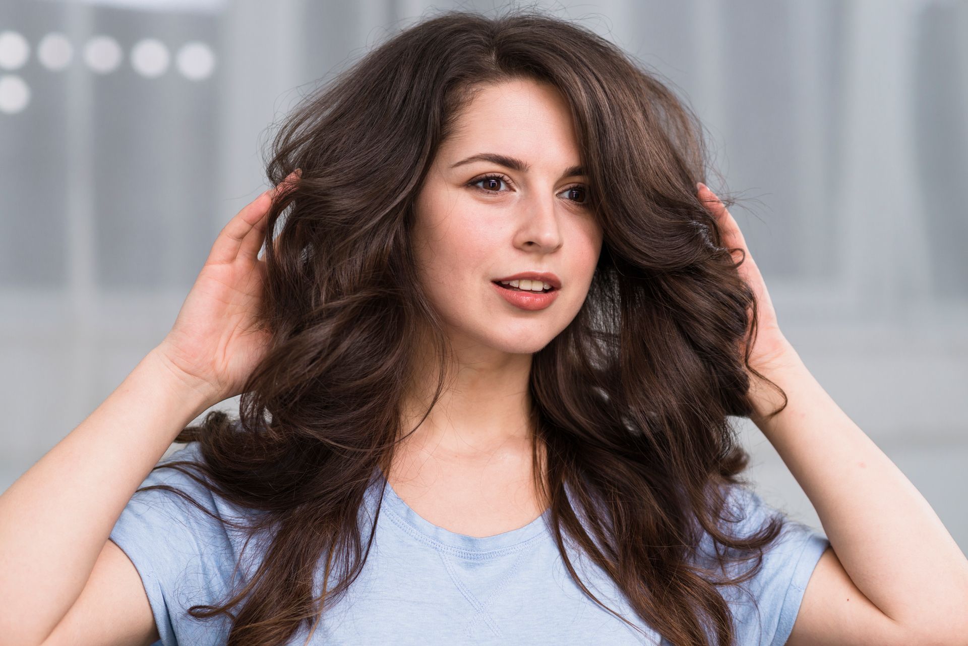 A woman in a blue shirt is touching her hair.