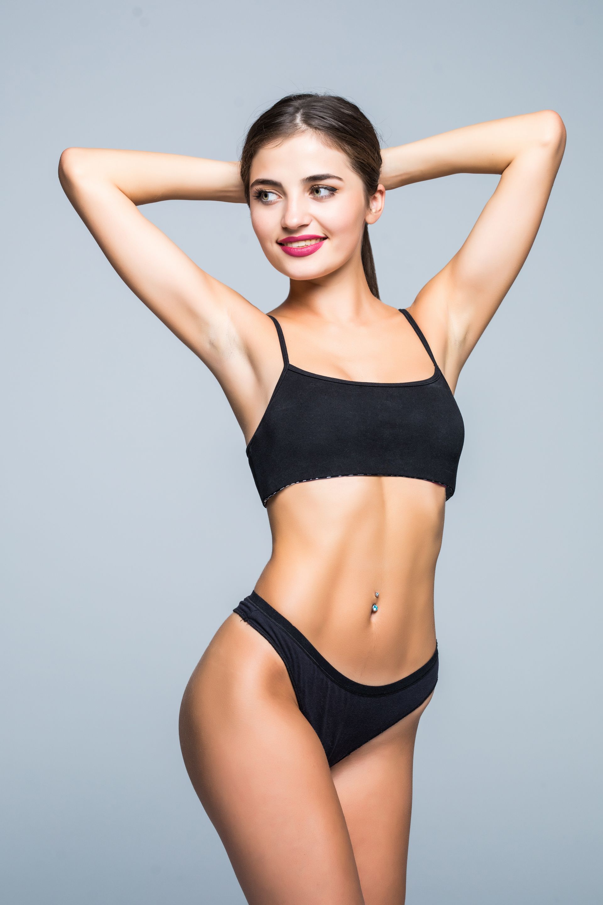 A woman in a black bikini is posing with her hands behind her head.