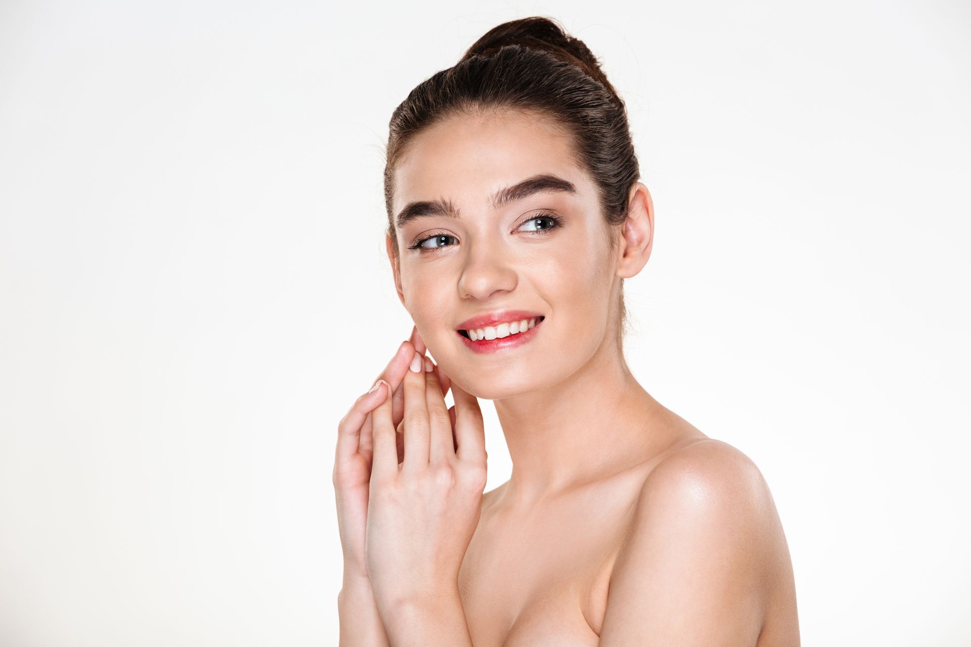 A young woman is smiling and touching her face.