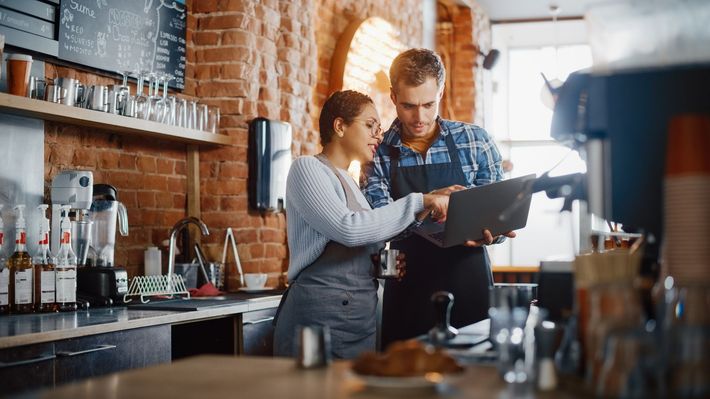 A man and a woman are looking at a laptop in a restaurant.