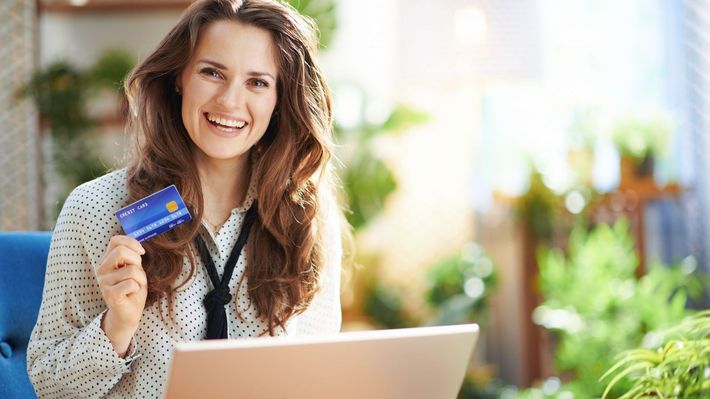 A woman is holding a credit card while using a laptop computer.