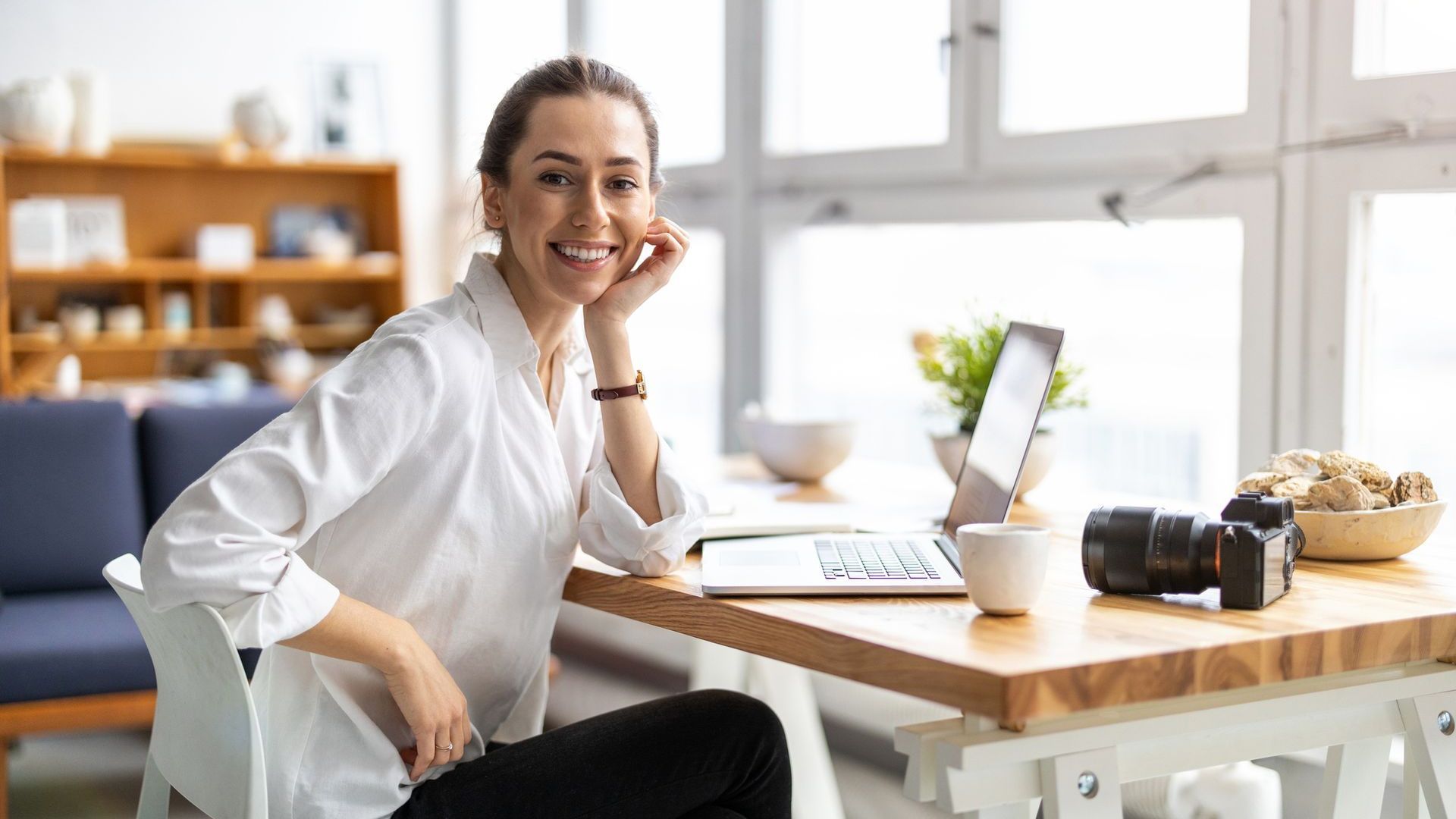 A woman is sitting at a table with a laptop and a camera.