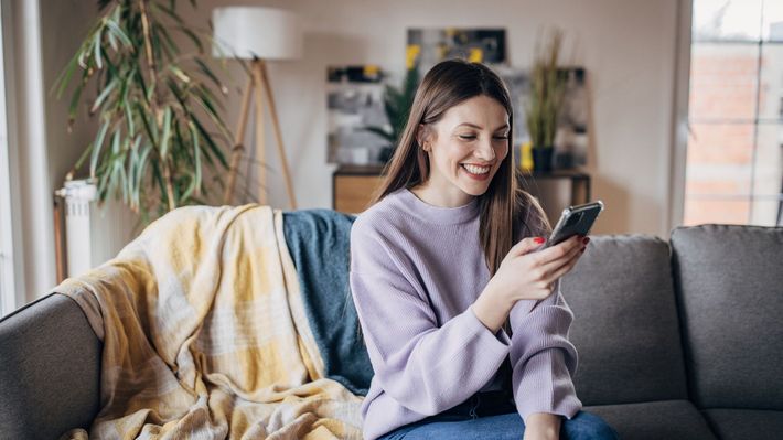 A woman is sitting on a couch looking at her cell phone.