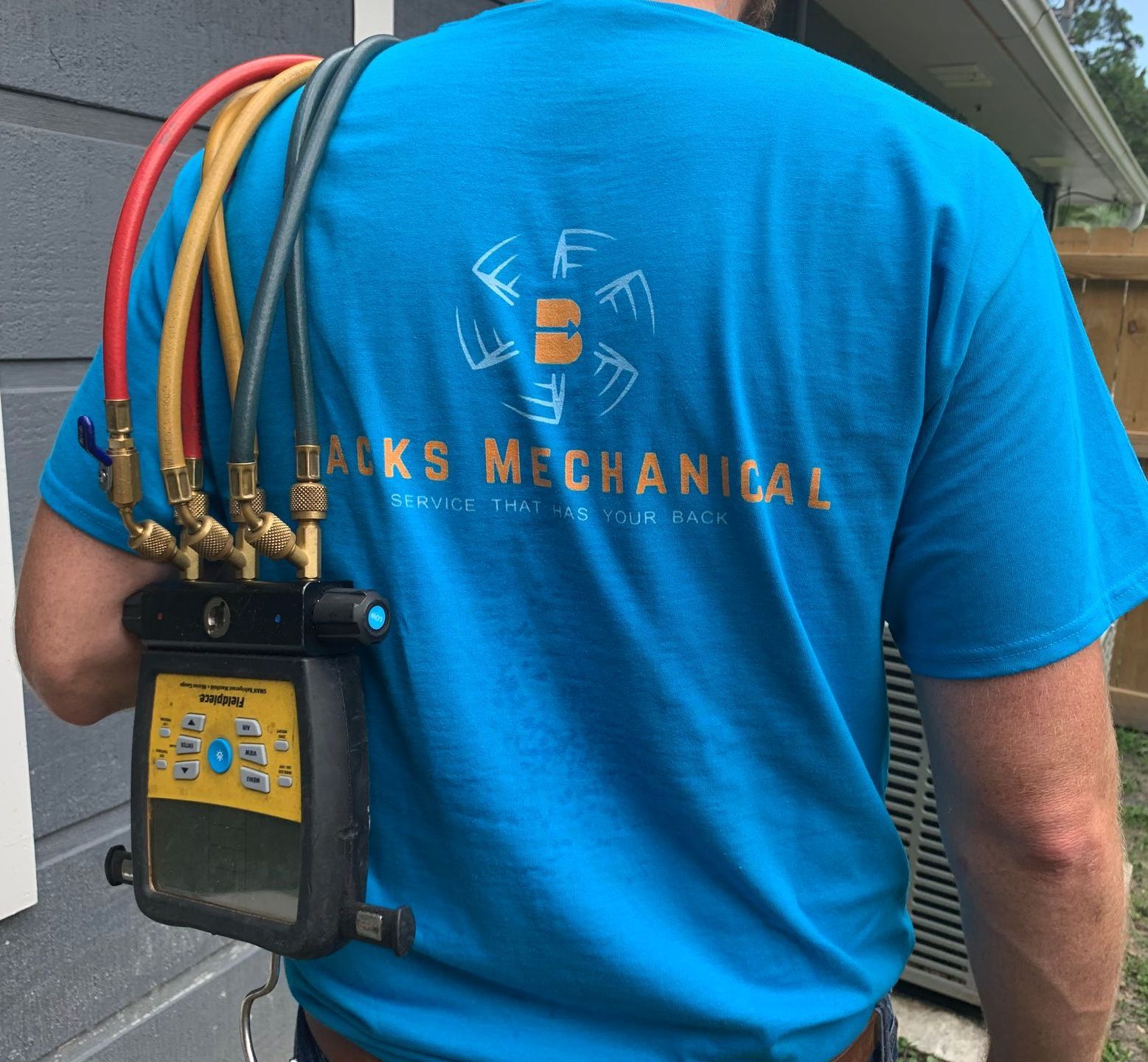 Rear image of a man holding a set of HVAC gauges over his shoulder