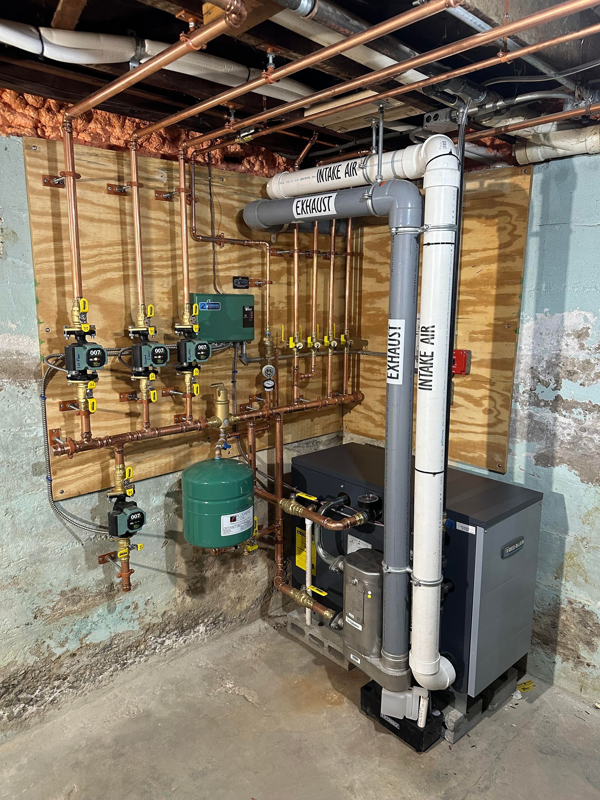 Copper pipes and green components of a heating system installed in a basement setting.