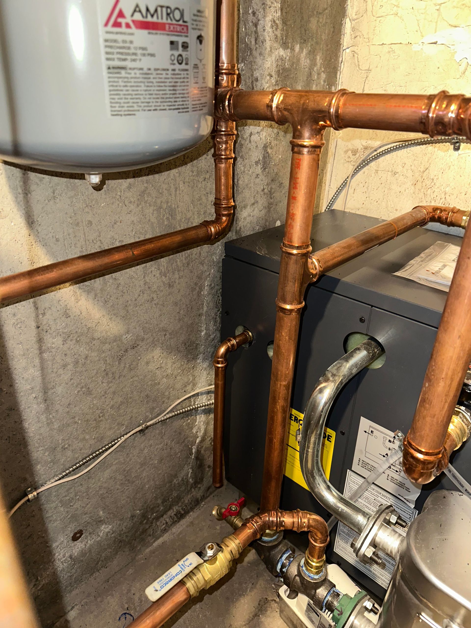 Copper pipes and fittings connected to a water heater and other components in a basement.