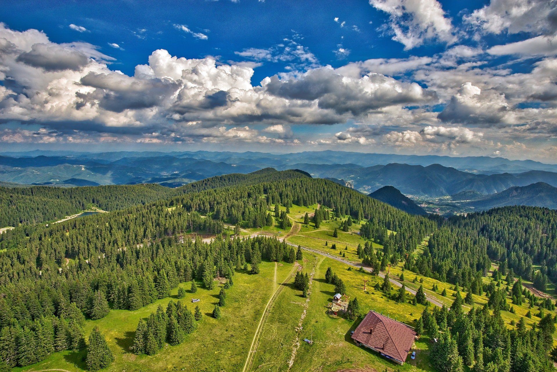 Aerial view of forested mountain landscape under a bright blue sky with puffy white clouds.