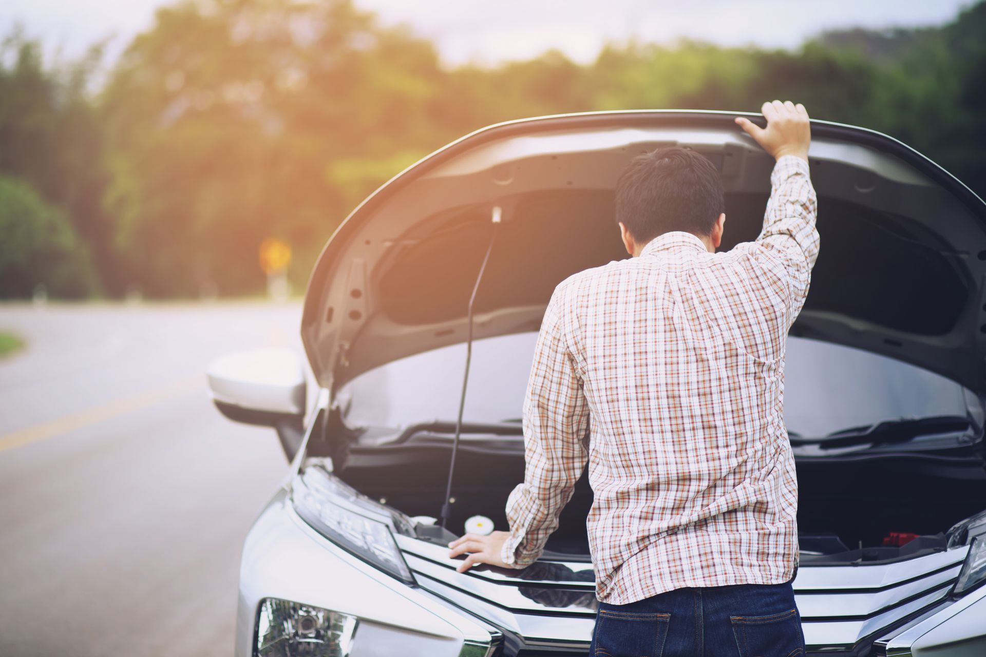View of a man opening the hood of his car on a road, waiting for road assistance.