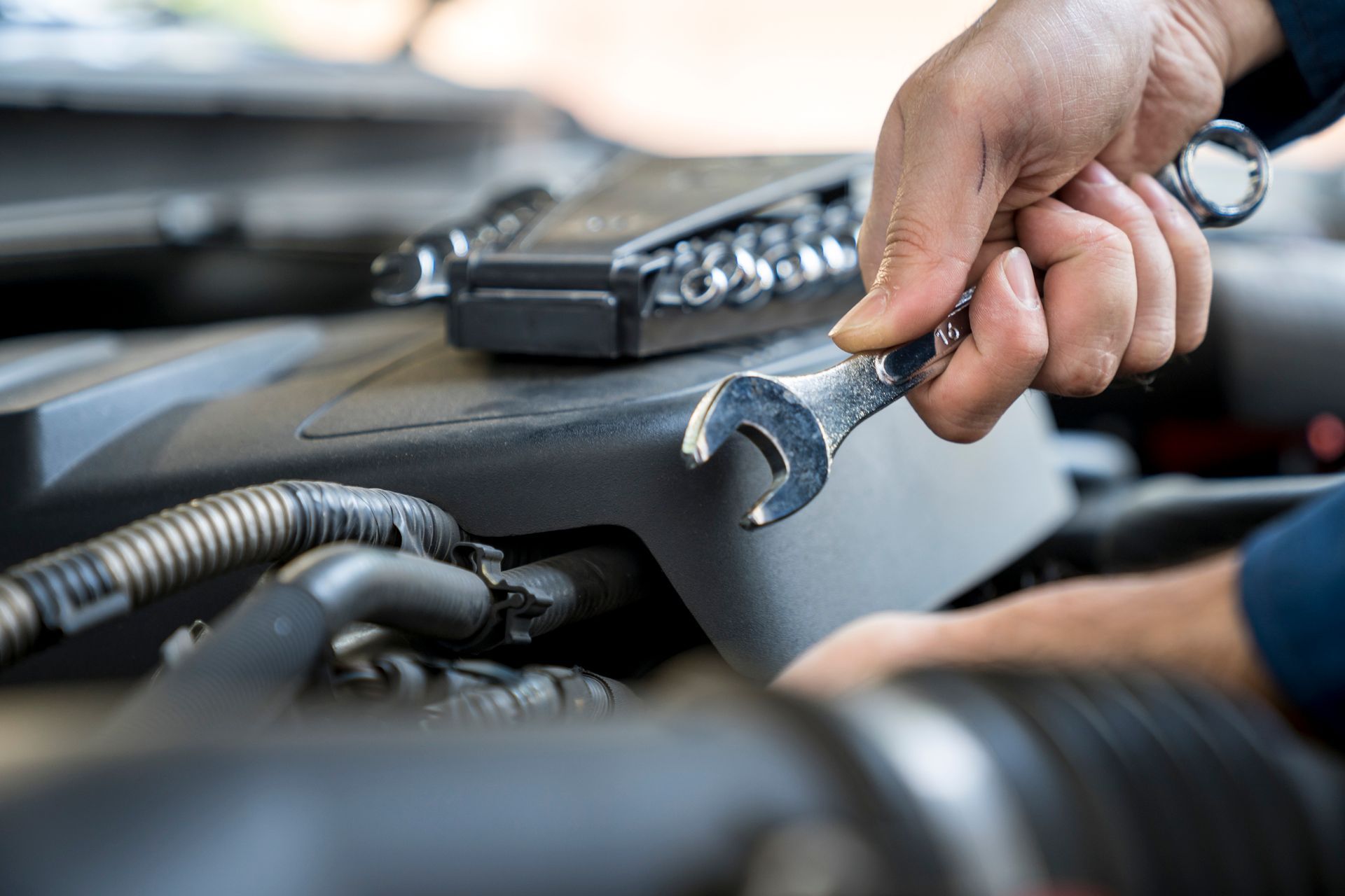 Close-up of a mechanic’s hands using a wrench while examining a car engine.