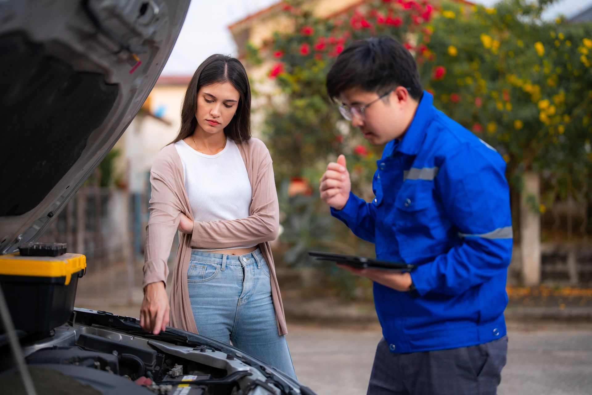 Mechanic with blue uniform fixing the car of a woman in the streets