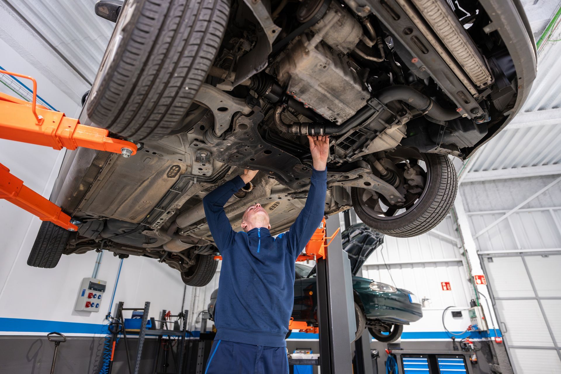 A man performs vehicle repair in a garage, surrounded by tools and car parts for maintenance.
