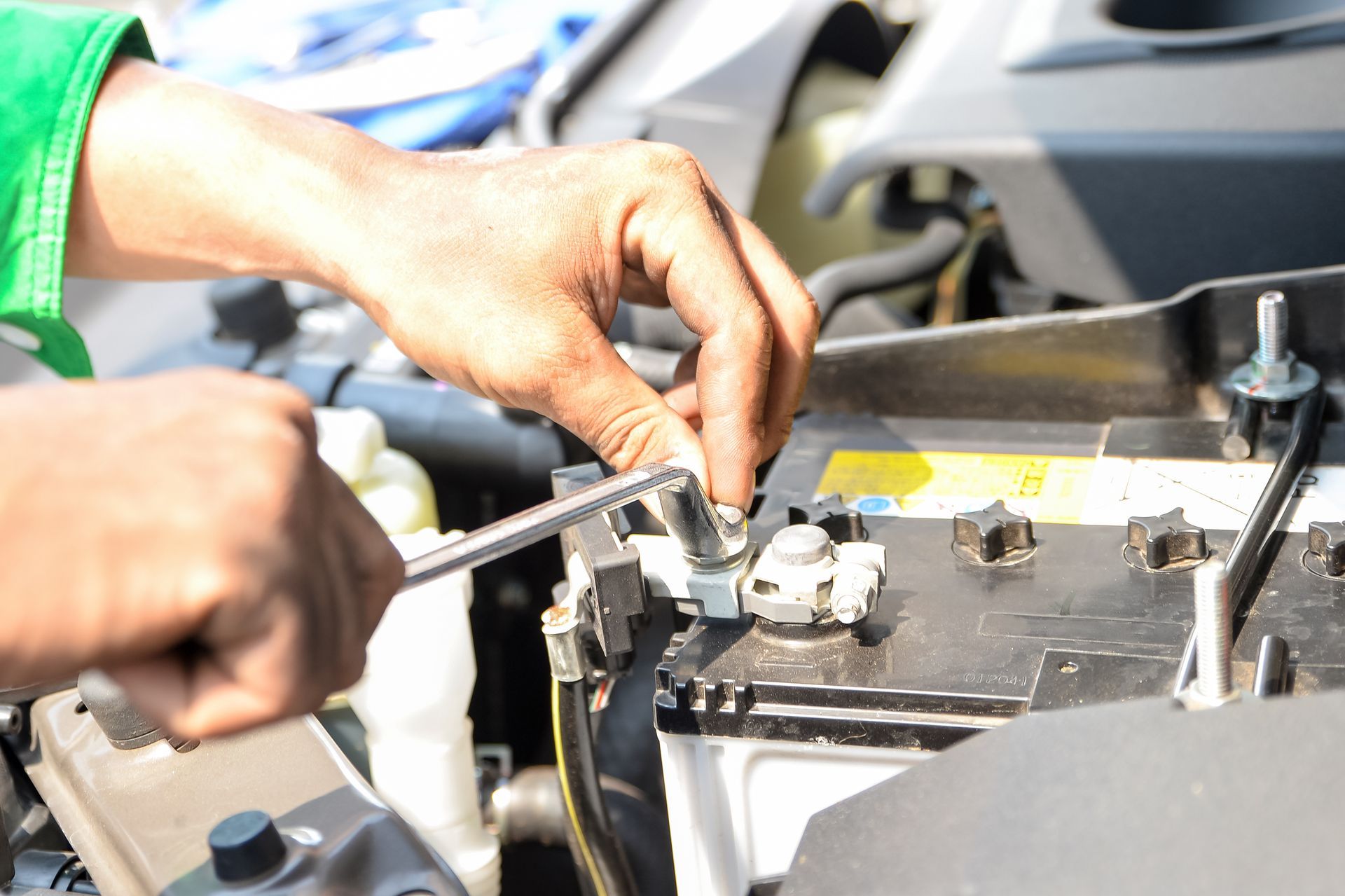 Close-up of hands while they fit a car’s battery screws, securing it to a car’s hood. Close-up of hands while they fit a car’s battery screws, securing it to a car’s hood.
