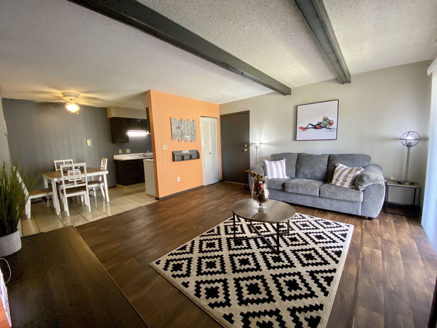Living room with gray sofa, patterned rug, wooden floors, and dining area.