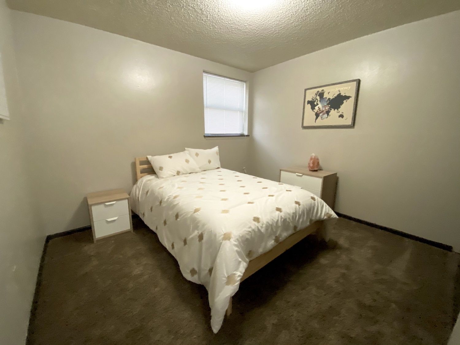 Bedroom with bed, nightstands, window, map art. Neutral colors. Brown carpet.