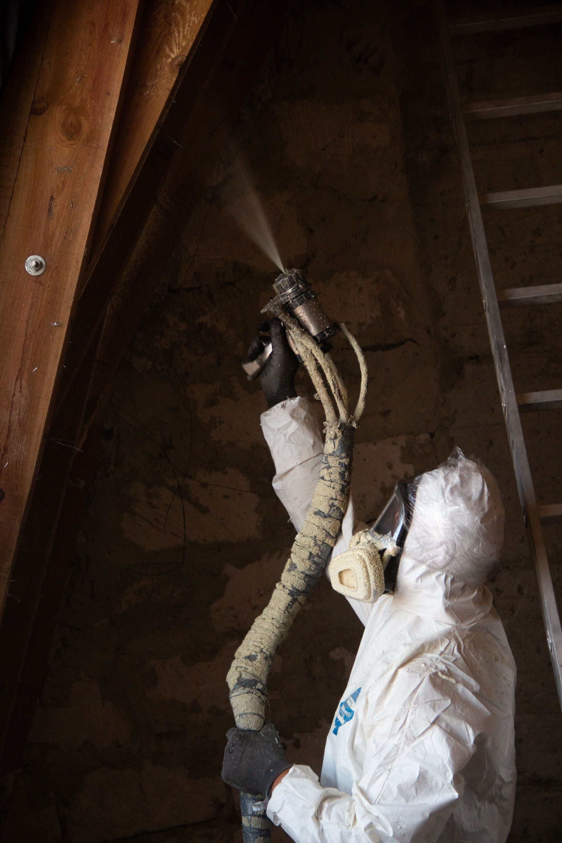 Person in protective suit spraying insulation into an attic.