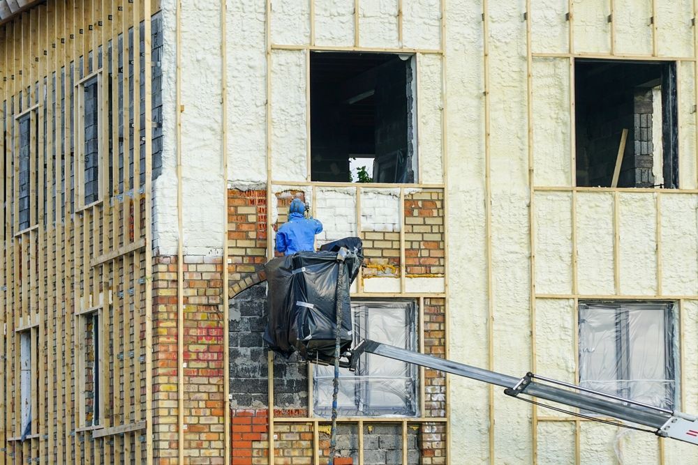 Construction worker in lift, spraying foam insulation on a building's exterior.
