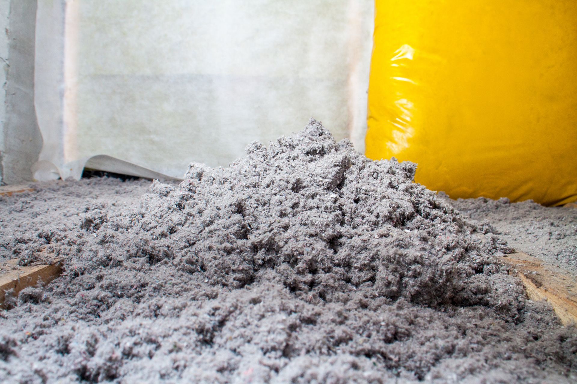 Pile of gray cellulose insulation on wooden beams, with yellow insulation visible in the background.