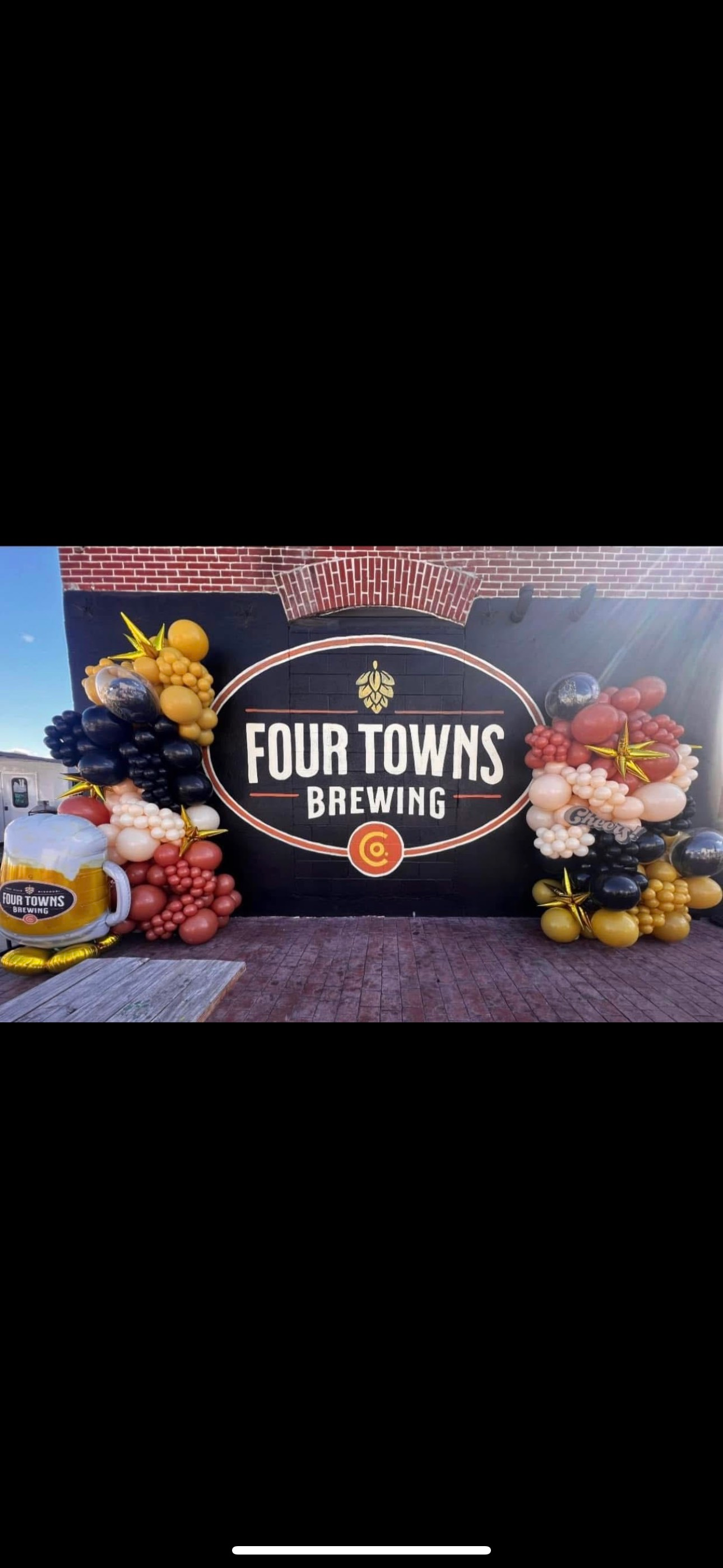 A sign for four towns brewing is surrounded by balloons.